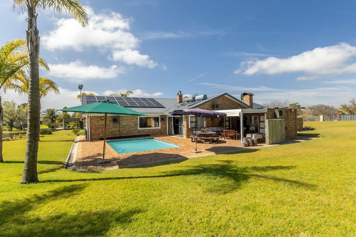 Rear view of the house featuring a brick facade, swimming pool, paved patio area, and roof-mounted solar panels set within a spacious garden.