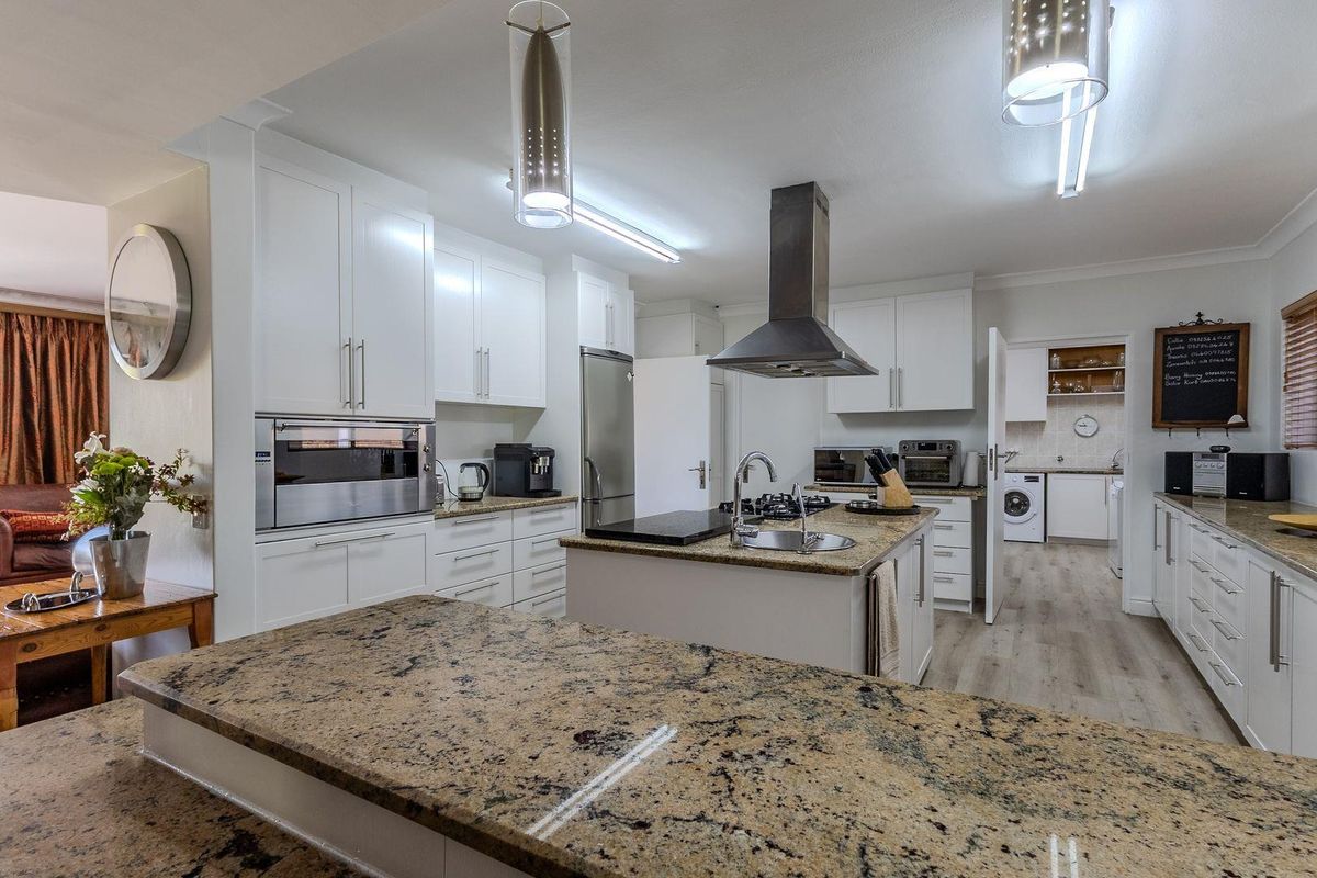 Modern kitchen featuring granite countertops, white cabinetry, a central island with a sink, and an adjoining scullery area with laundry facilities.