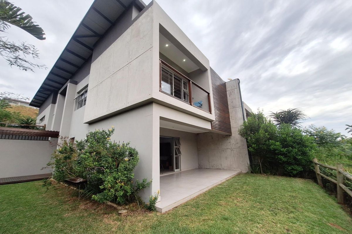 Modern rear elevation featuring a covered patio, upper-level balcony, concrete and timber facade finishes, and a well-maintained garden area.