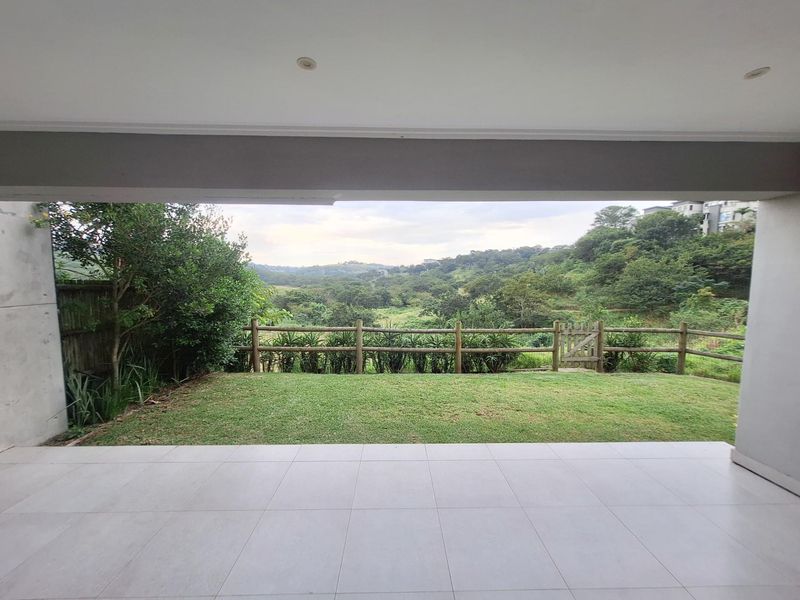 A covered patio featuring light-colored floor tiles and recessed lighting, overlooking a private lawn and scenic natural landscape.