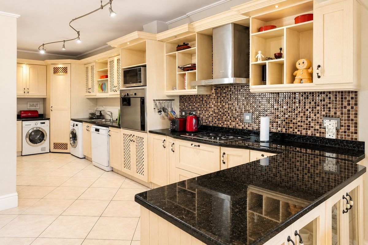 Spacious kitchen featuring light wood cabinetry, dark granite countertops, mosaic tile backsplash, and integrated laundry facilities with modern track lighting.