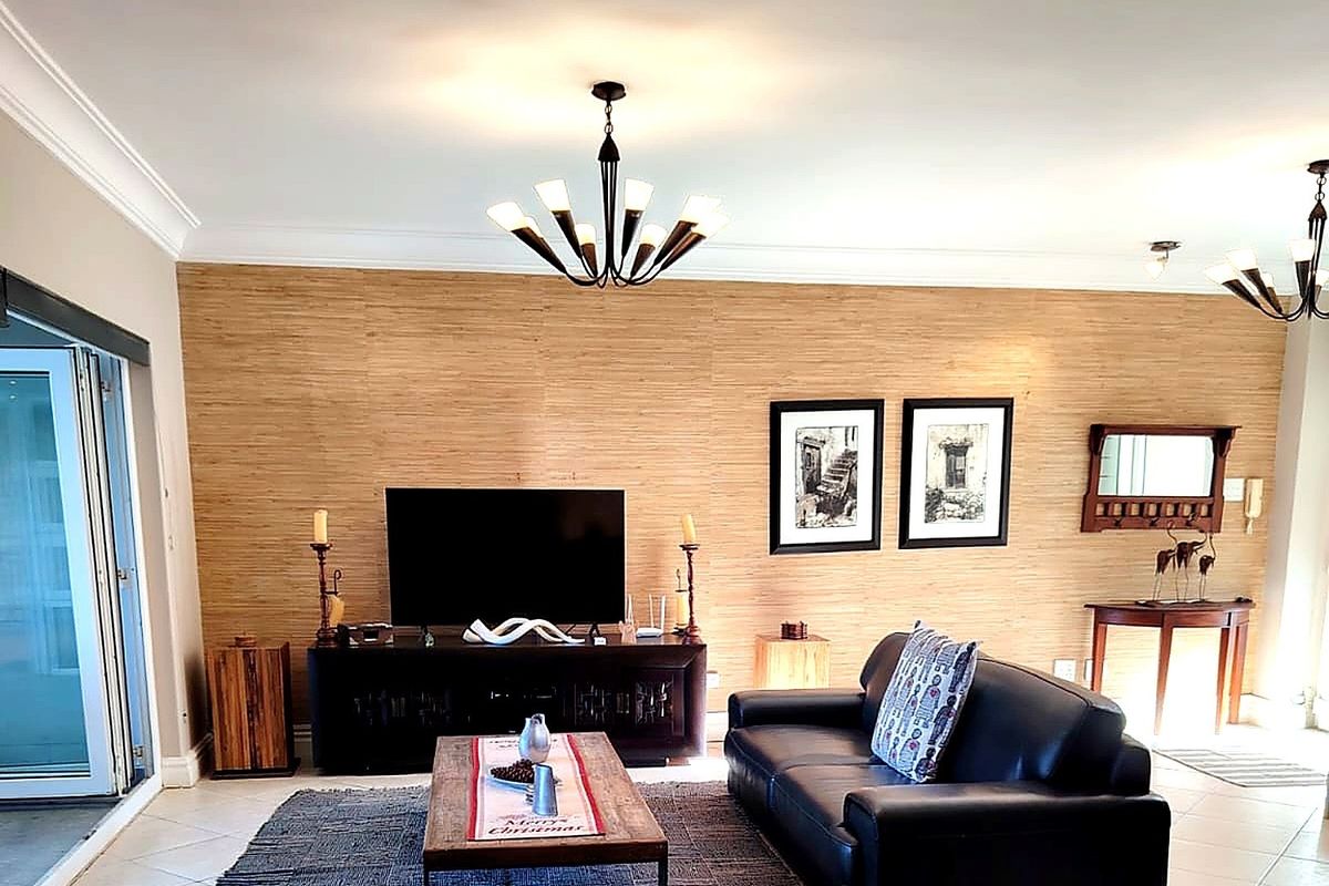 A well-maintained living room featuring textured bamboo-style wall cladding, crown molding, tiled flooring, and direct access to an outdoor patio through sliding glass doors.