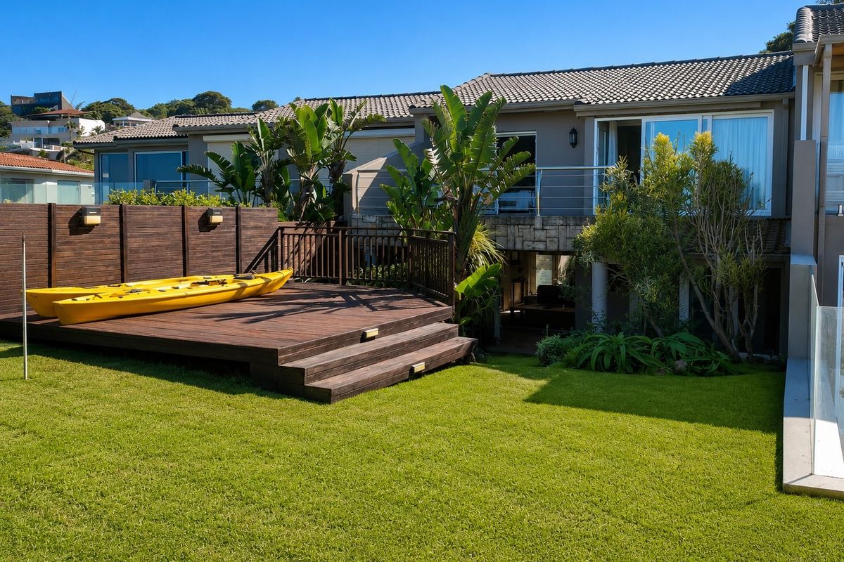 A well-maintained rear exterior featuring a raised timber deck, landscaped lawn, and a balcony with modern stainless steel railings overlooking the garden.