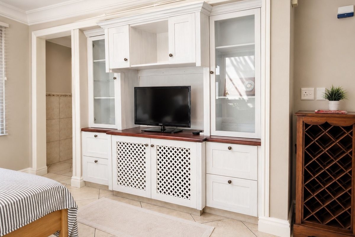 A bedroom featuring custom built-in white cabinetry with glass display sections and a dark wood countertop, complemented by tiled flooring and crown molding.