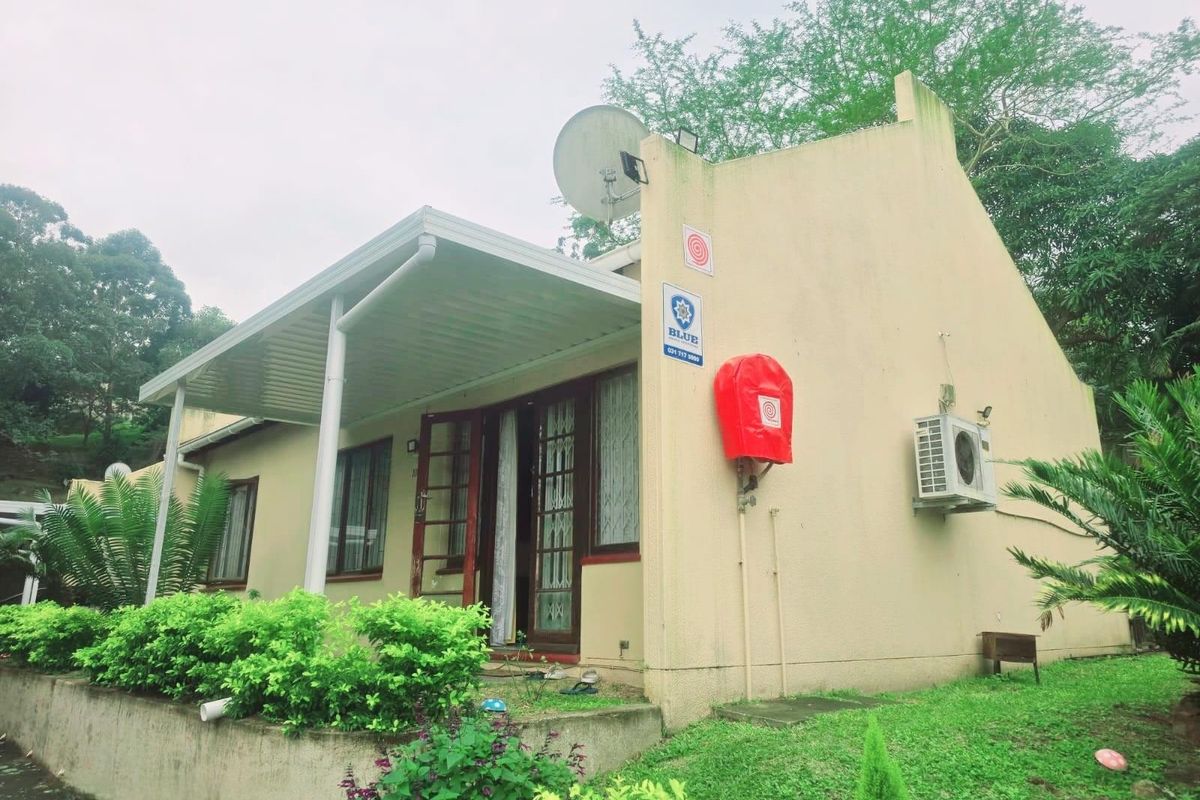 Rear exterior view of the townhouse featuring a covered patio, security alarm system, external fire hose reel, and wall-mounted air conditioning unit.
