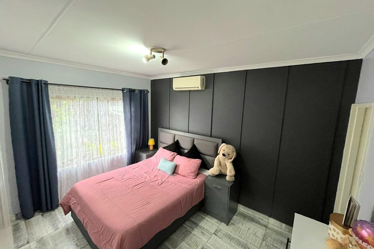 A well-maintained bedroom featuring a dark accent wall, split-system air conditioning, and tiled flooring, offering a modern and comfortable living space.
