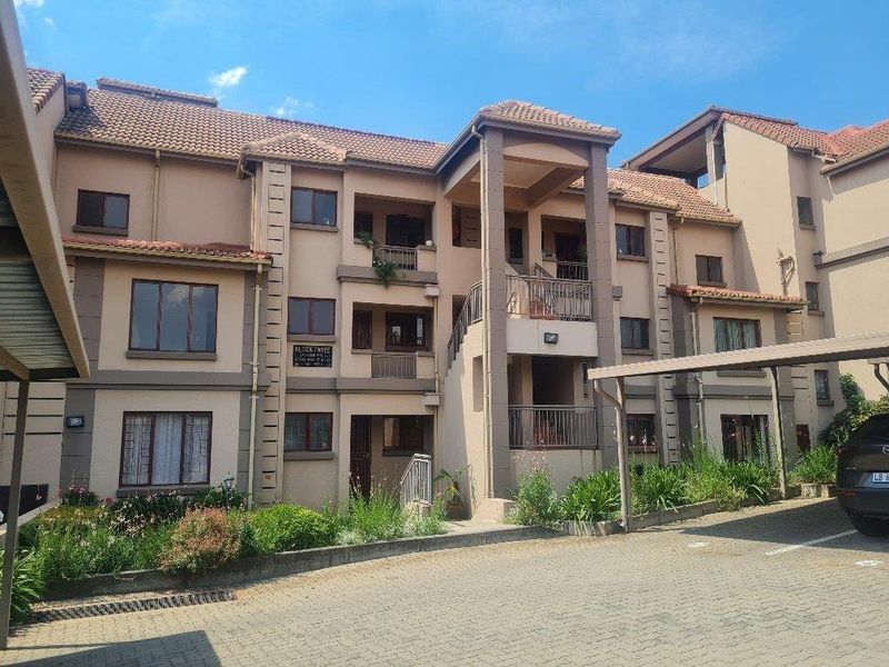 Exterior view of a multi-story townhouse complex featuring tiled roofing, paved parking area, and covered carports.