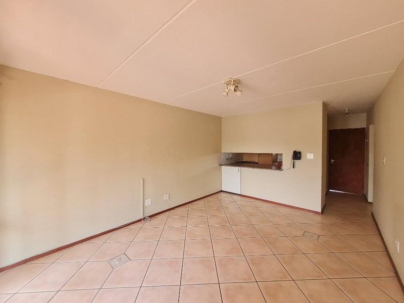 An open-plan living area featuring tiled flooring, neutral walls, and a pass-through window connecting to the kitchen space.