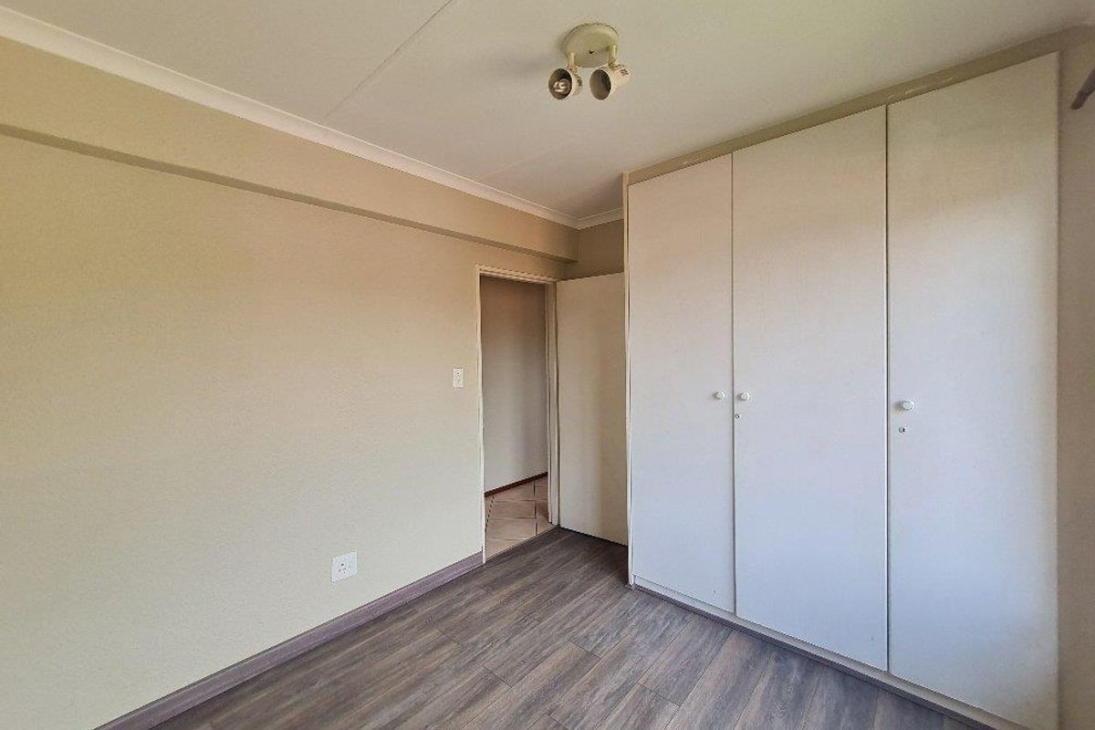 A bedroom featuring wood-look laminate flooring, neutral wall tones, and built-in floor-to-ceiling wardrobes with white doors.