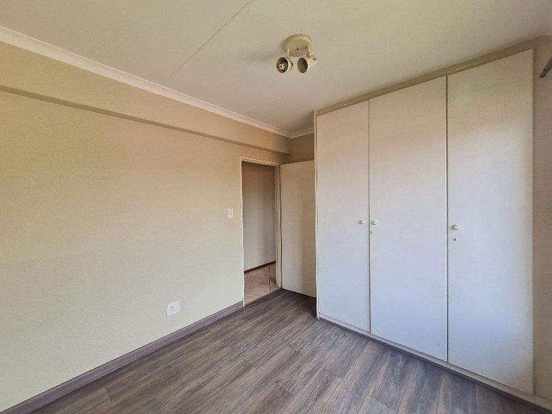 A bedroom featuring wood-look laminate flooring, neutral wall tones, and built-in floor-to-ceiling wardrobes with white doors.