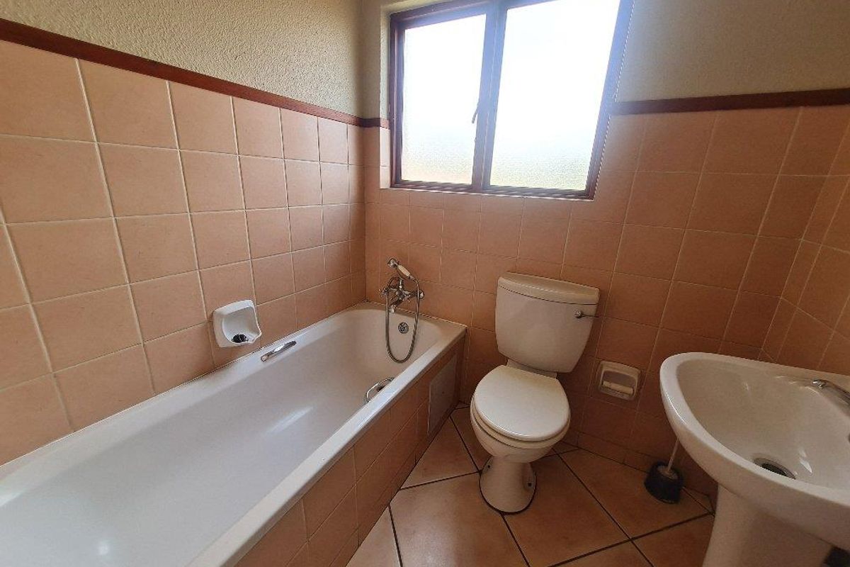 A functional bathroom featuring a built-in bathtub, pedestal basin, and toilet with classic peach-toned wall tiles and tiled flooring.