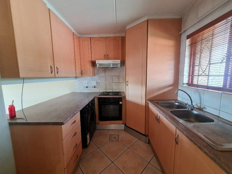 A functional kitchen featuring wood-tone cabinetry, a built-in oven with hob, extractor fan, and a double stainless steel sink with tiled splashbacks.