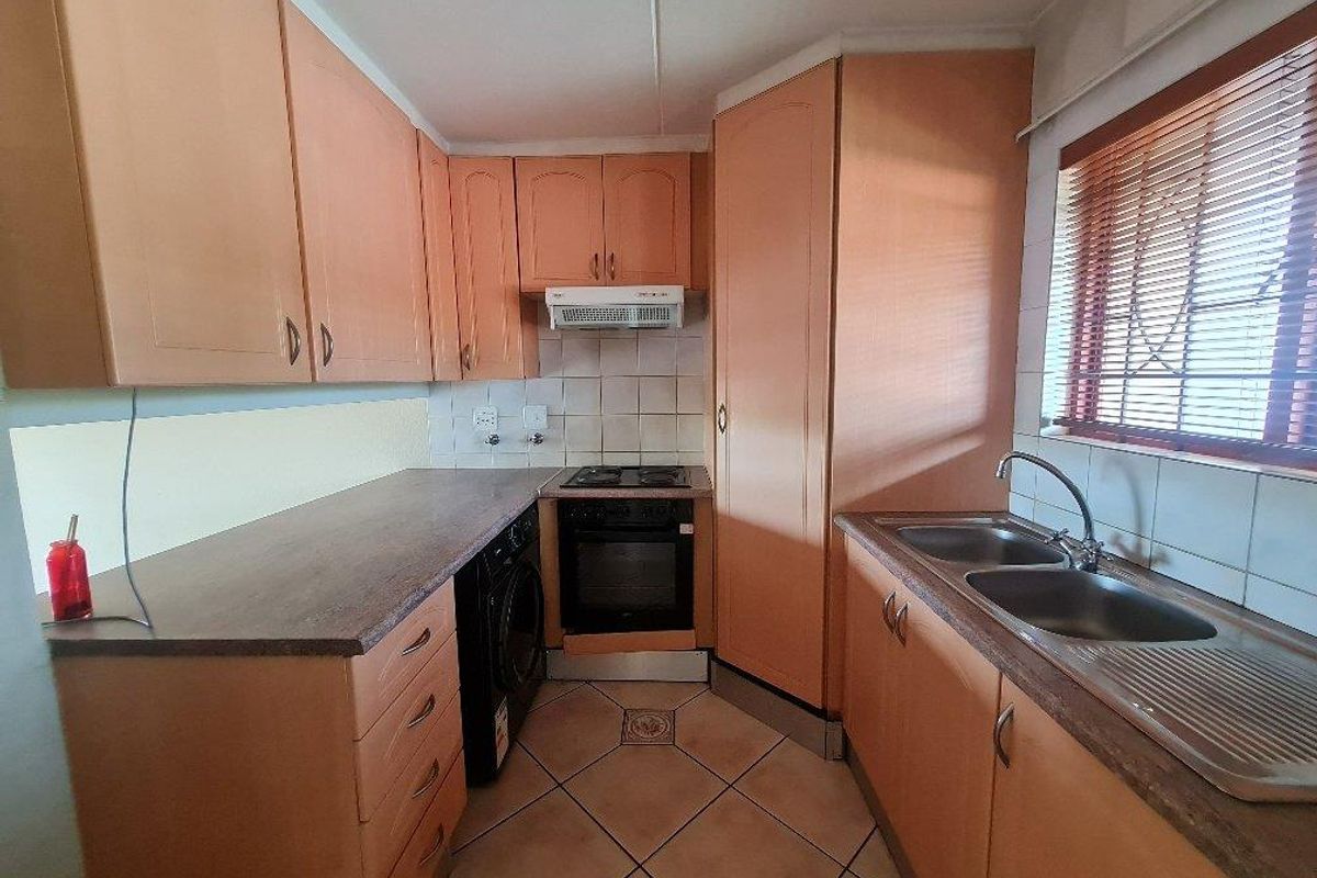 A functional kitchen featuring wood-tone cabinetry, a built-in oven with hob, extractor fan, and a double stainless steel sink with tiled splashbacks.