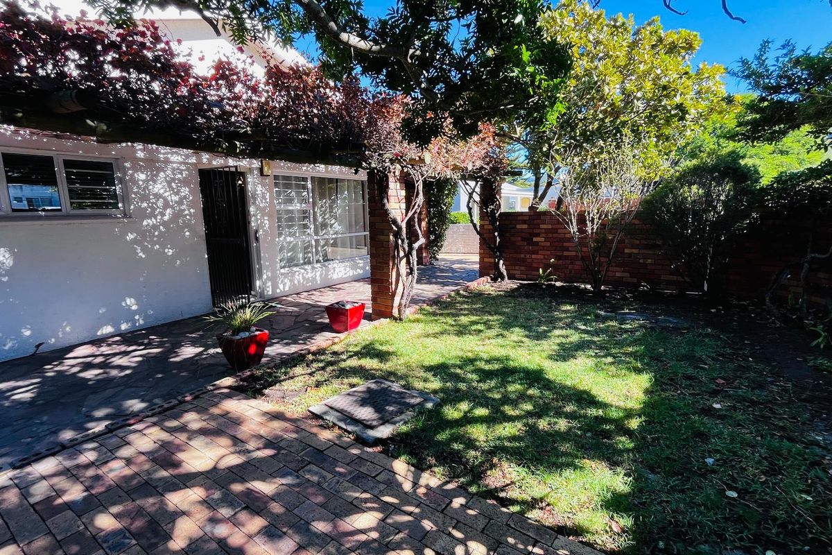 A private rear garden featuring a paved patio area, a pergola structure, and a brick boundary wall, offering a quiet outdoor space.
