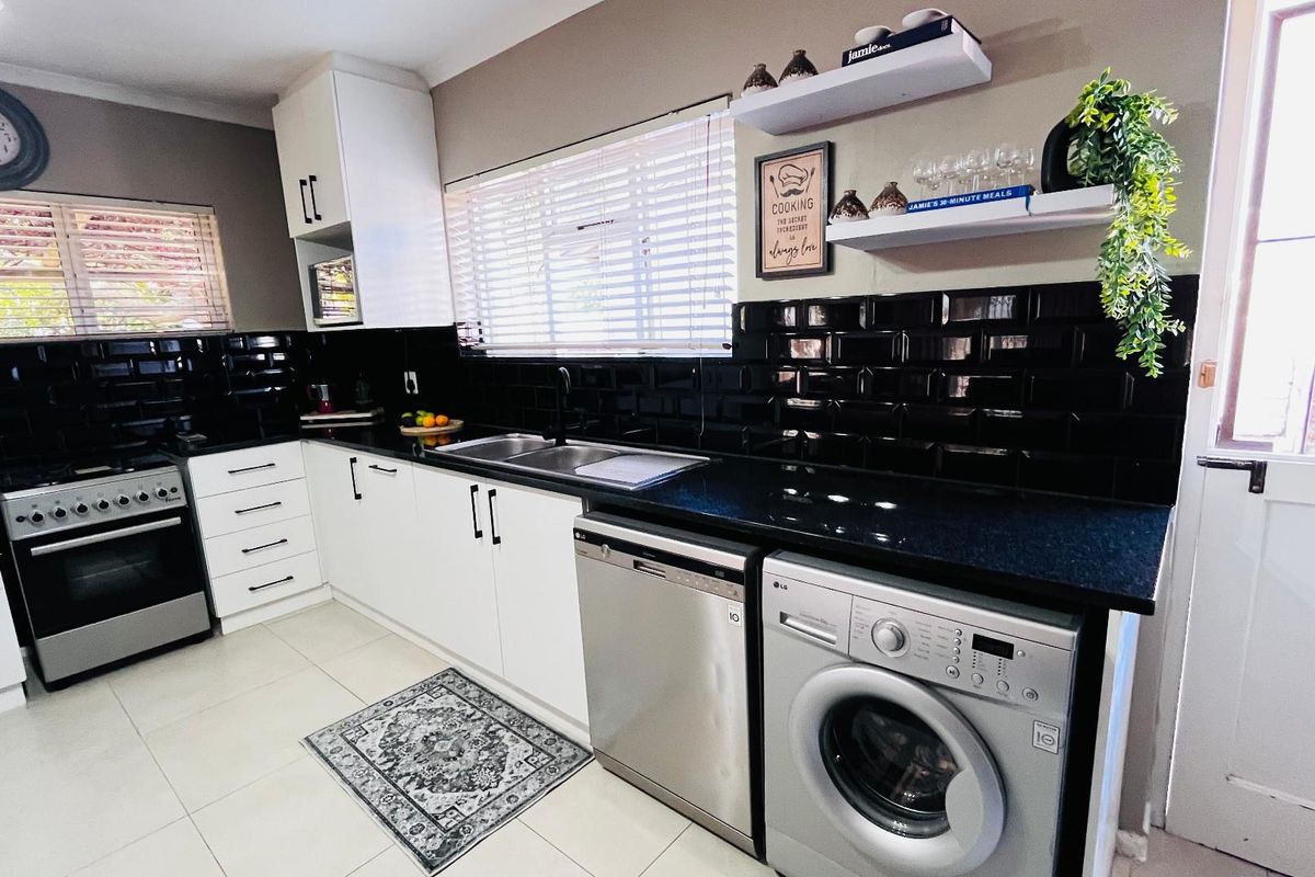 Modern kitchen featuring white cabinetry, black subway tile backsplash, granite countertops, and integrated stainless steel appliances.