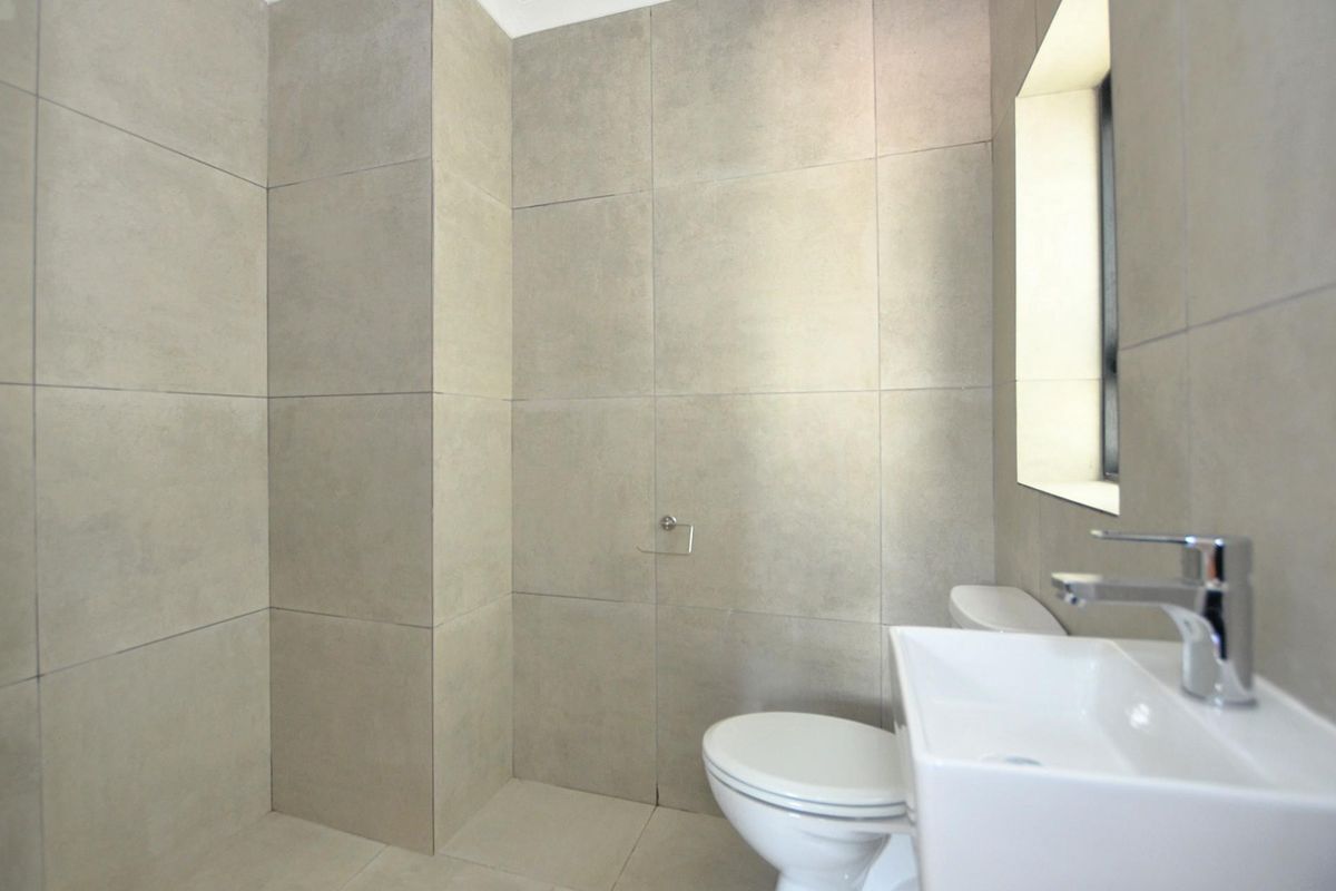 A modern bathroom featuring large-format neutral wall tiles, a contemporary basin with chrome mixer tap, and a wall-mounted toilet.