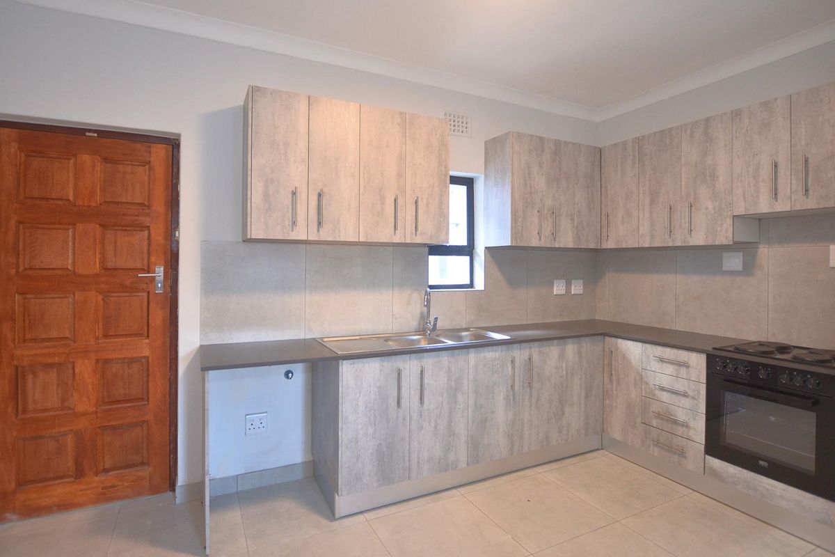 Modern kitchen featuring light wood-grain cabinetry, stone-look countertops, a built-in oven and hob, and tiled flooring.