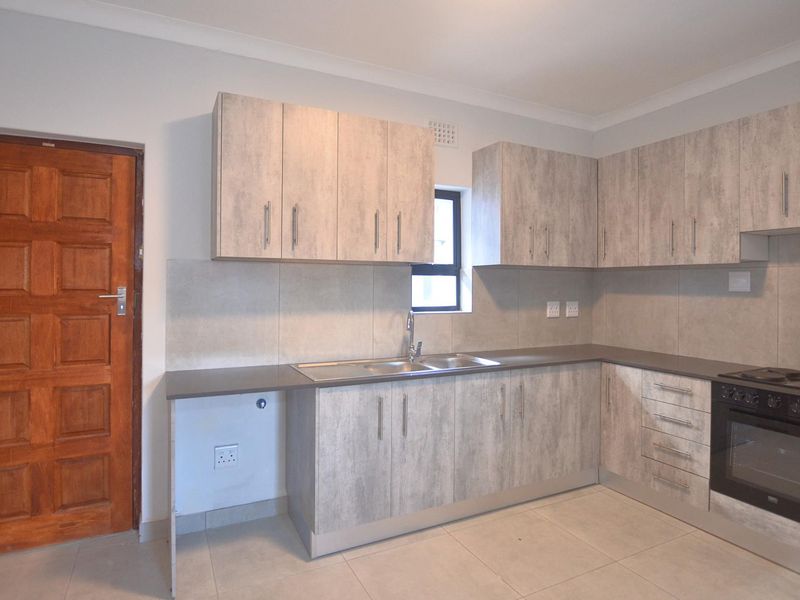 Modern kitchen featuring light wood-grain cabinetry, stone-look countertops, a built-in oven and hob, and tiled flooring.