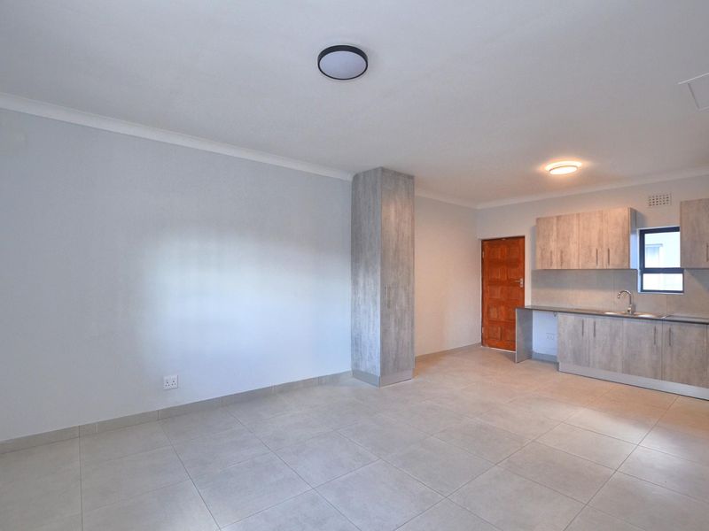 An open-plan living area featuring modern light-wood cabinetry, a stainless steel sink, tiled flooring, and a built-in storage cupboard.