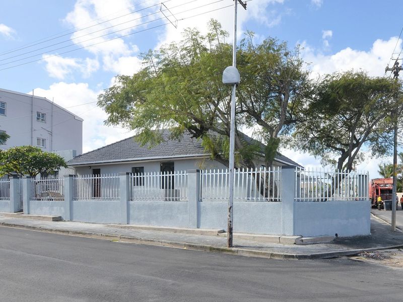A corner-lot residential property featuring a perimeter wall with metal fencing, a tiled roof, and established trees within the front garden area.