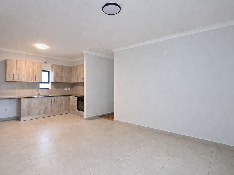 An open-plan kitchen featuring light wood-look cabinetry, tiled flooring, and a built-in oven, seamlessly flowing into a spacious living area.