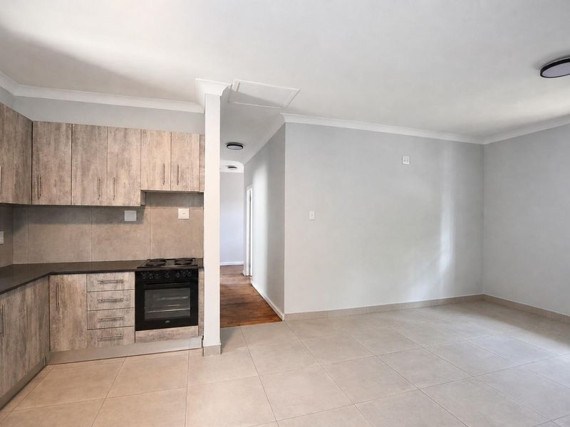 Open plan kitchen featuring modern wood-look cabinetry, built-in oven and hob, and tiled flooring, seamlessly flowing into the adjacent living area.
