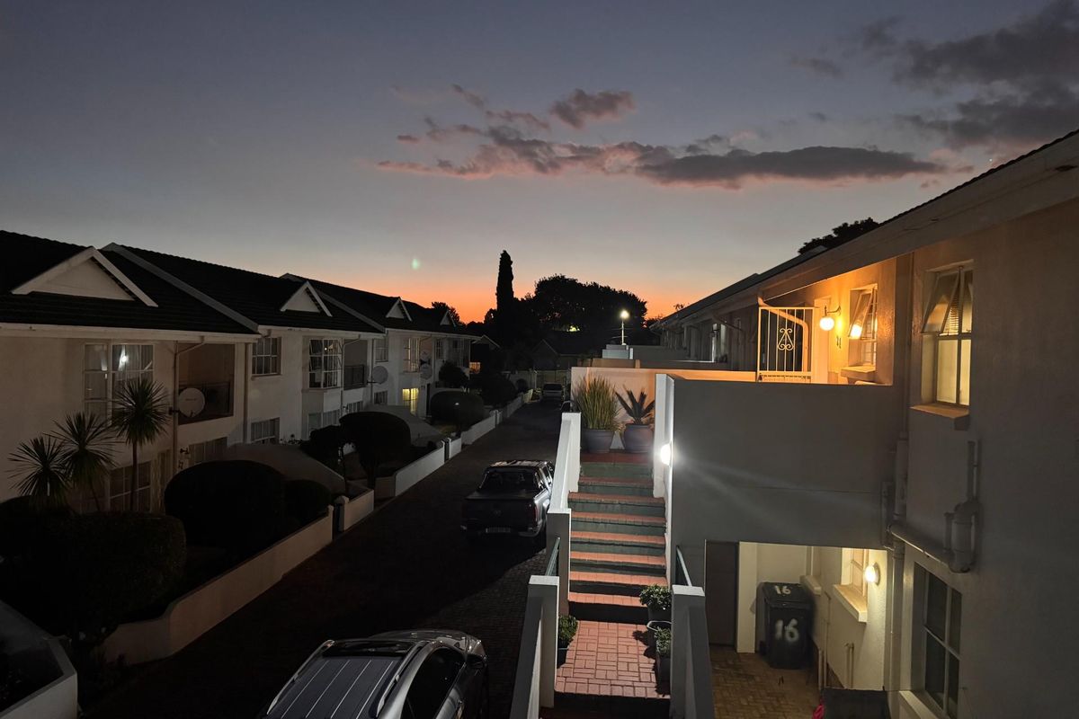 An evening view of an apartment complex exterior featuring a paved driveway, external staircase, and balcony access under a sunset sky.