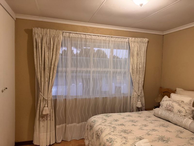 A cozy bedroom featuring laminate flooring, a built-in wardrobe, and a large window with classic drapery, offering a comfortable and functional living space.