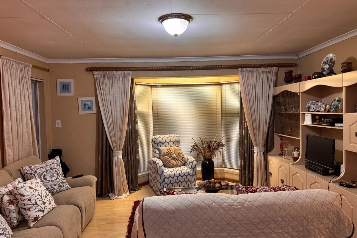 A cozy living room featuring a prominent bay window with blinds, laminate flooring, and neutral wall tones.