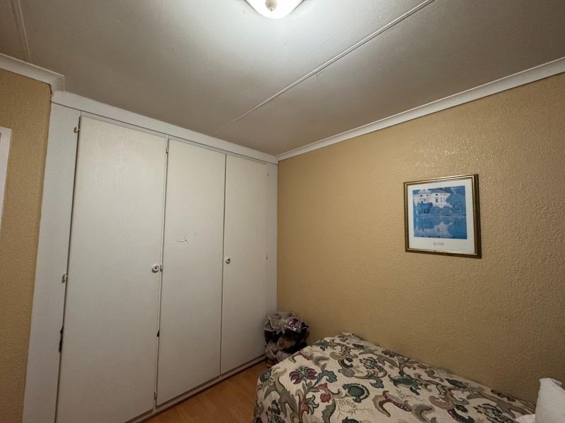 A bedroom featuring built-in wardrobes, laminate flooring, and cove cornicing, offering a functional space with potential for cosmetic updates.