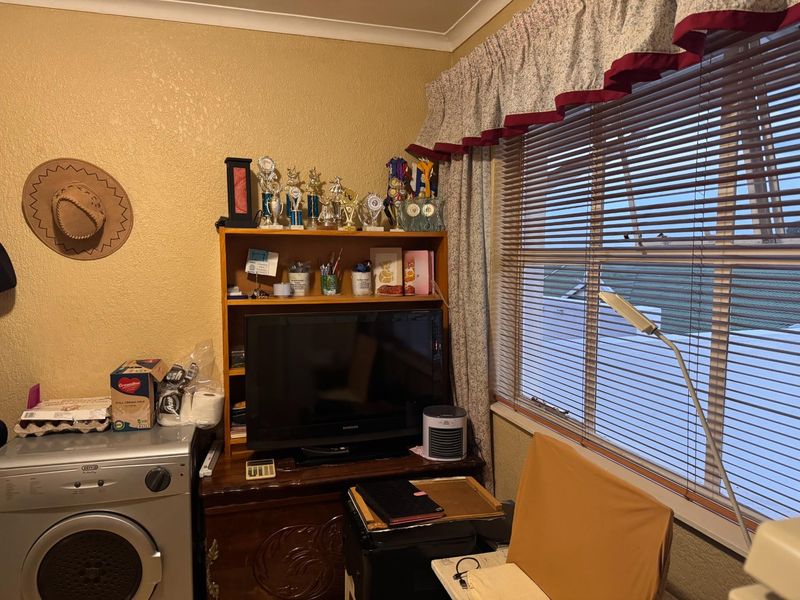 A functional laundry area featuring a built-in washing machine, window with venetian blinds, and decorative curtain pelmet.