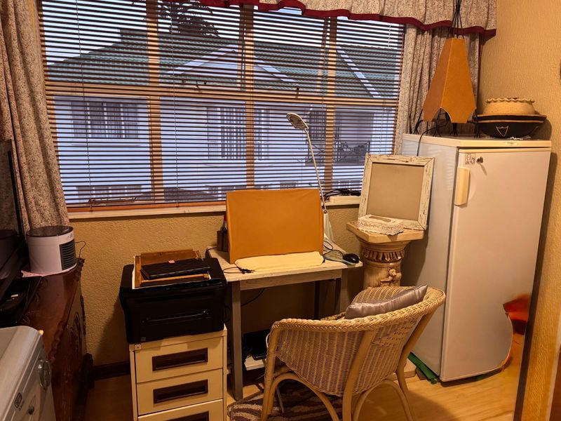 A bedroom space featuring laminate flooring and window treatments, currently utilized as a home office area.
