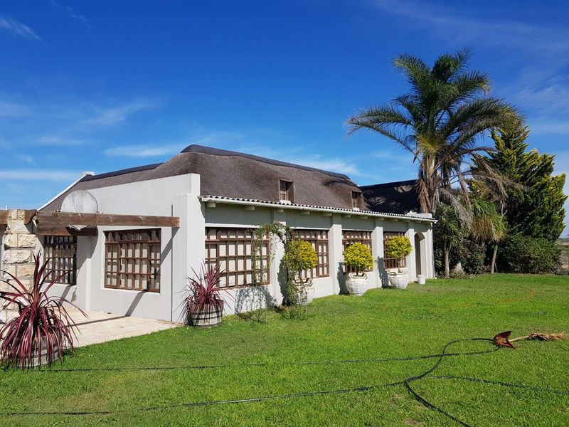 A well-maintained farm-style residence featuring a traditional thatched roof, timber-framed windows, and a paved patio area set within a spacious garden.