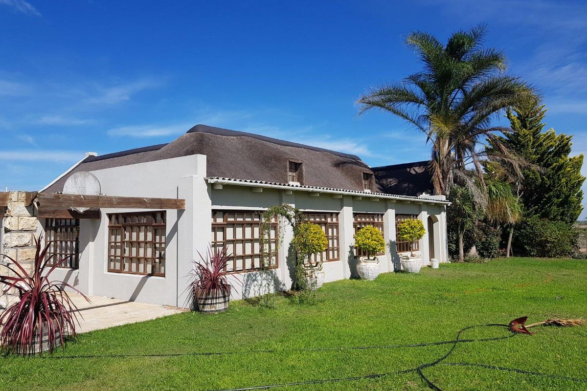 A well-maintained farm-style residence featuring a traditional thatched roof, timber-framed windows, and a paved patio area set within a spacious garden.