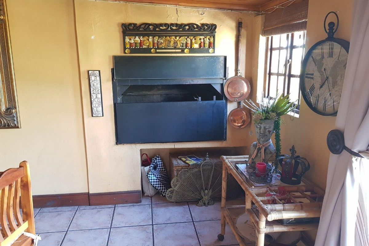 A rustic living area featuring a built-in indoor fireplace, tiled flooring, and timber ceiling beams, creating a cozy and traditional atmosphere.