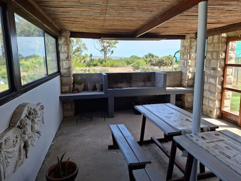 Covered outdoor patio featuring a built-in braai area, stone masonry pillars, and expansive views of the surrounding farm landscape.