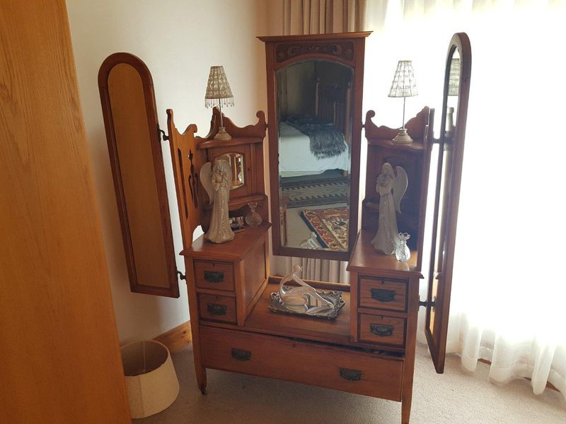 A bedroom interior featuring a classic wooden vanity unit with integrated mirrors and drawers, positioned near a window with natural light.
