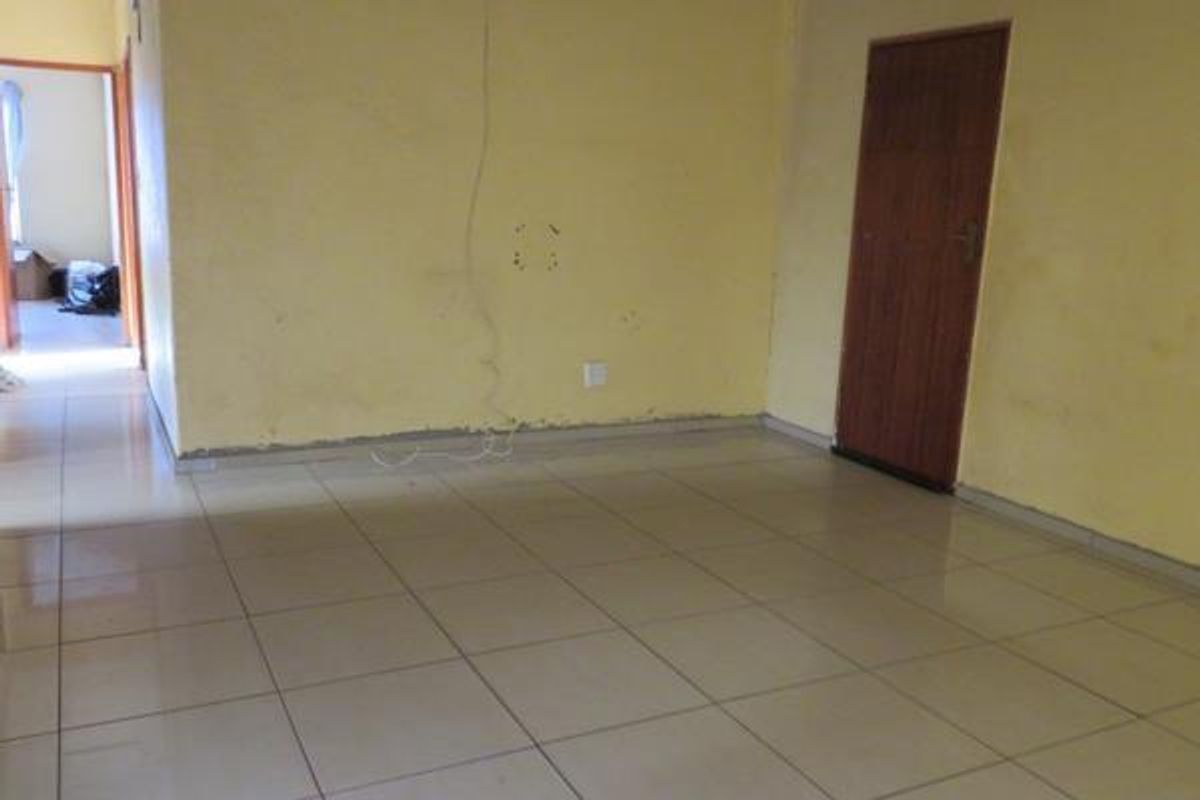 An empty living room featuring tiled flooring, a wooden door, and yellow painted walls requiring cosmetic attention.