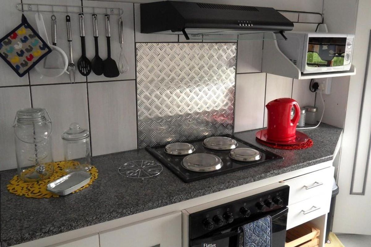 A compact kitchen area featuring a built-in electric stove, oven, extractor fan, and a metal splashback with tiled walls and granite-look countertops.