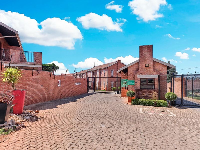 The entrance to Bushmill complex featuring a secure guard house, brick boundary walls with electric fencing, and a paved driveway.