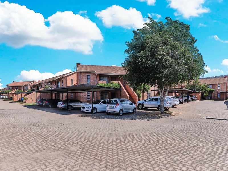 Exterior view of a brick apartment complex featuring covered parking bays and a paved driveway area.