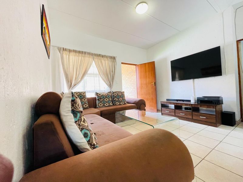 A functional living room featuring tiled flooring, neutral walls, and direct access to an exterior area through a wooden door.