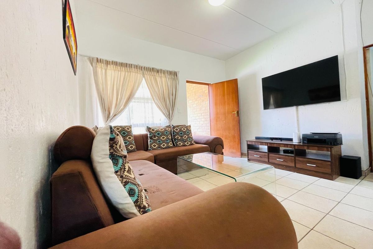 A functional living room featuring tiled flooring, neutral walls, and direct access to an exterior area through a wooden door.