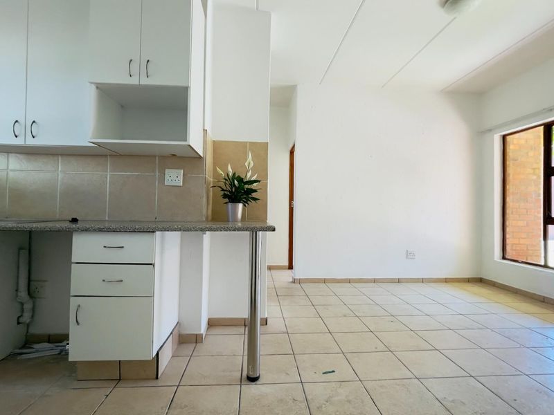 An open-plan kitchen and living area featuring tiled flooring, built-in white cabinetry, and a large window providing natural light.