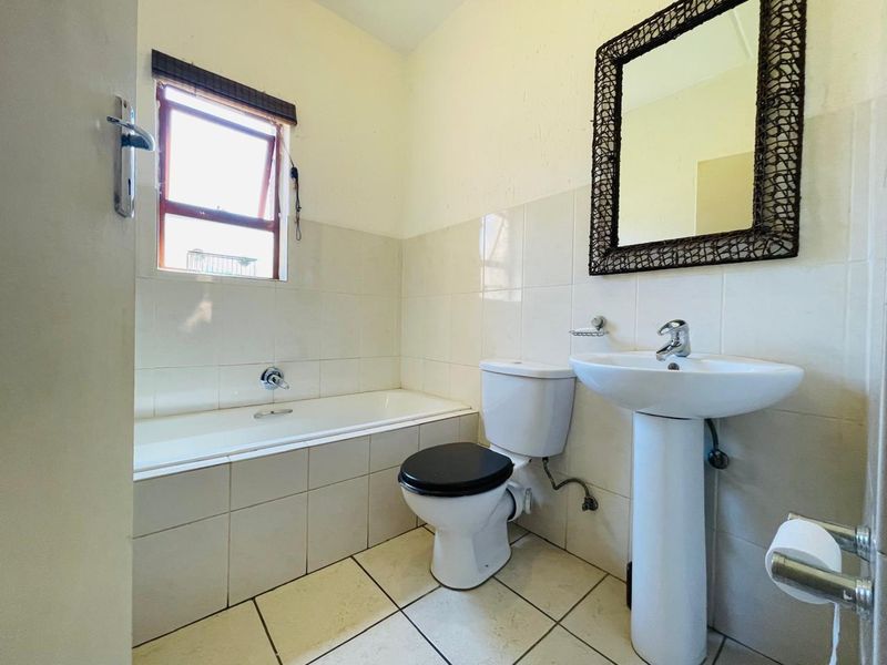 A functional bathroom featuring a pedestal basin, toilet, and bathtub with neutral wall and floor tiling.