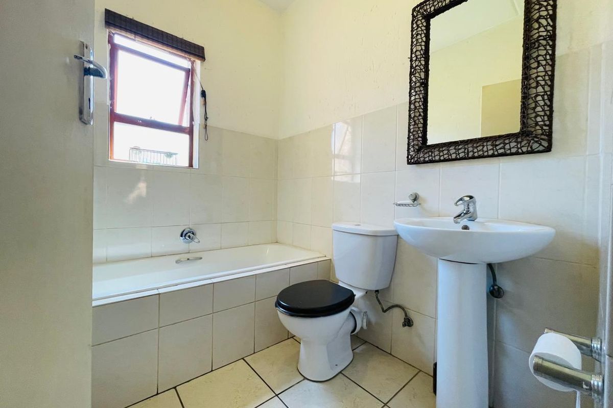 A functional bathroom featuring a pedestal basin, toilet, and bathtub with neutral wall and floor tiling.