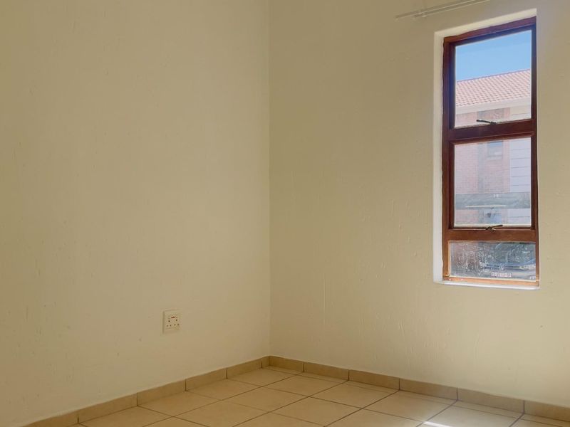A bright, empty bedroom featuring neutral tiled flooring and a timber-framed window, providing a clean canvas for personalization.