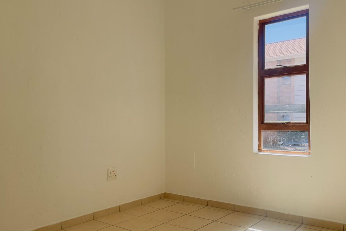 A bright, empty bedroom featuring neutral tiled flooring and a timber-framed window, providing a clean canvas for personalization.