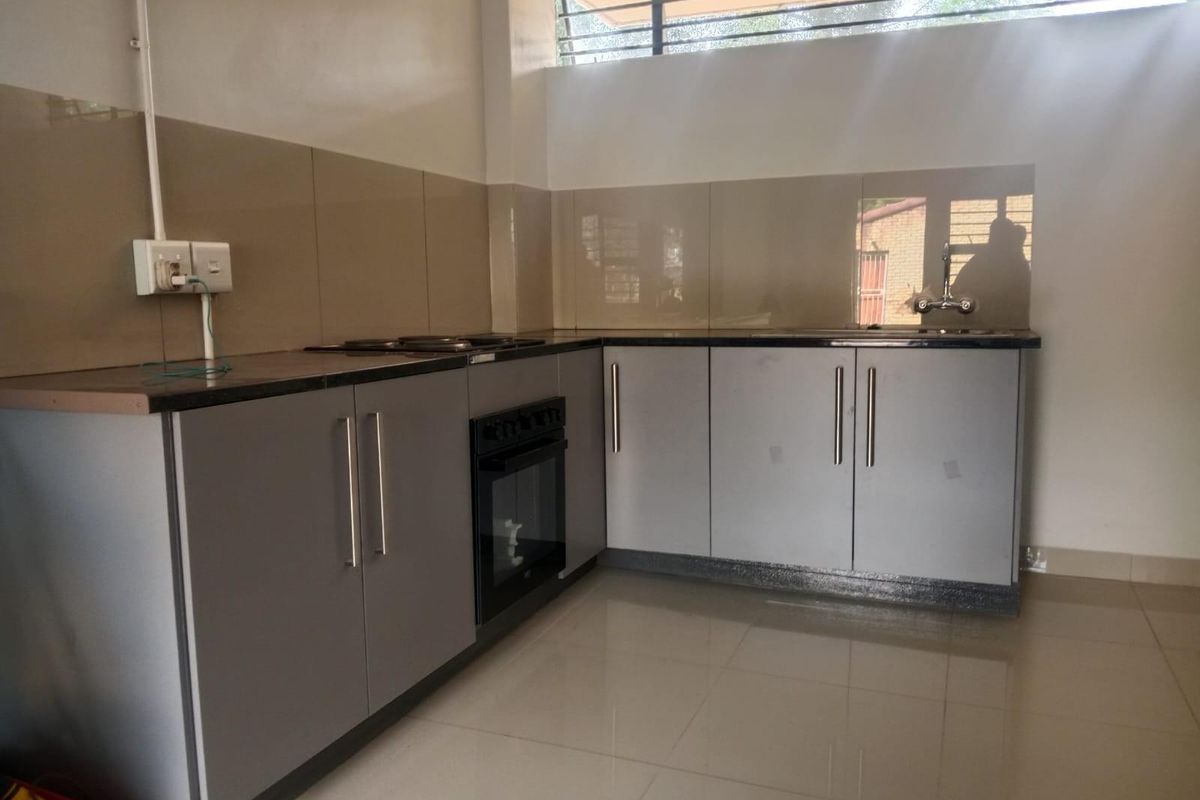 A functional kitchen featuring grey cabinetry, dark countertops, a built-in oven, hob, and tiled splashbacks with neutral floor tiles.