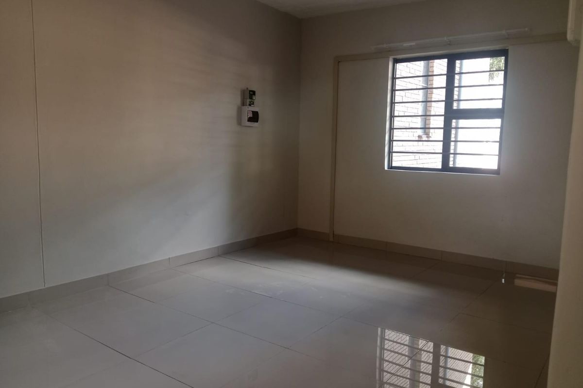 A vacant, neutrally painted room featuring large format floor tiles, a window with security bars, and an electrical distribution board.